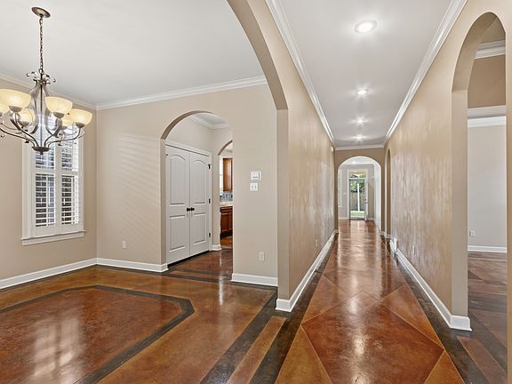 Lovely front entrance hall. Attention to detail is evident in the custom concrete floors, smooth ceilings, and arched doorways. The dining room is visible to the left. New washer/dryer behind double doors. View of middle bedroom on the Right.