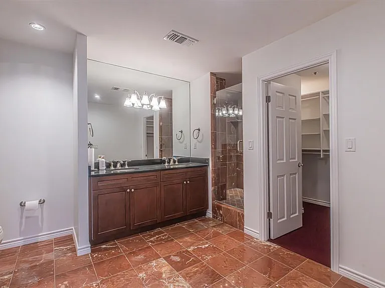 Bathroom featuring a double vanity with dark cabinetry and countertop, an expansive wall mirror, a glass-enclosed shower with matching tile, and red-toned floor tiles