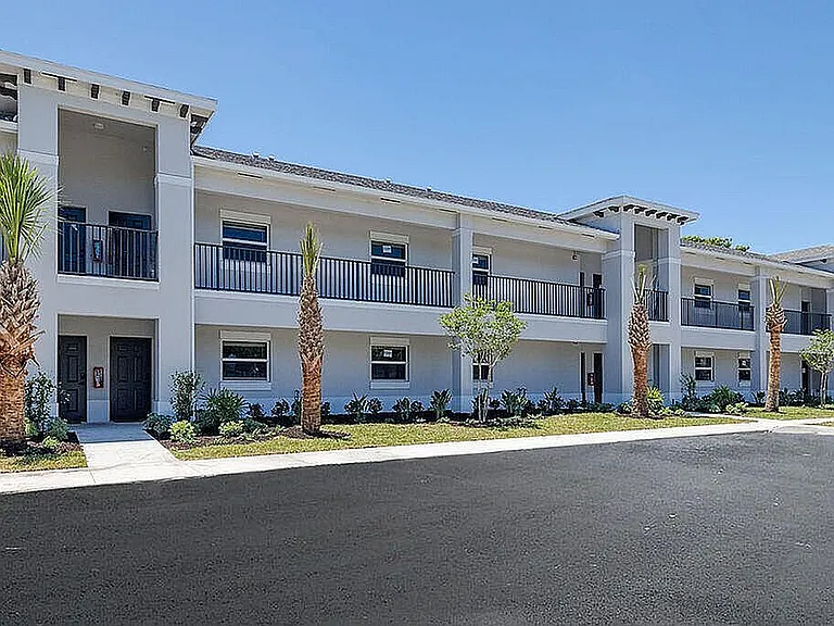 Elegant two-story apartment building with modern design, large windows, and lush landscaping under a clear blue sky.