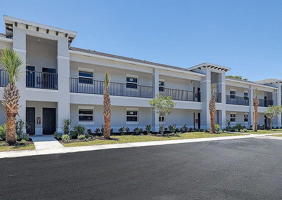 Elegant two-story apartment building with modern design, large windows, and lush landscaping under a clear blue sky.