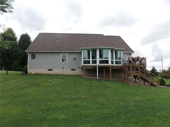 View from the rear includes the enclosed sunroom and side deck with stairs to the above ground pool and lower level patio.