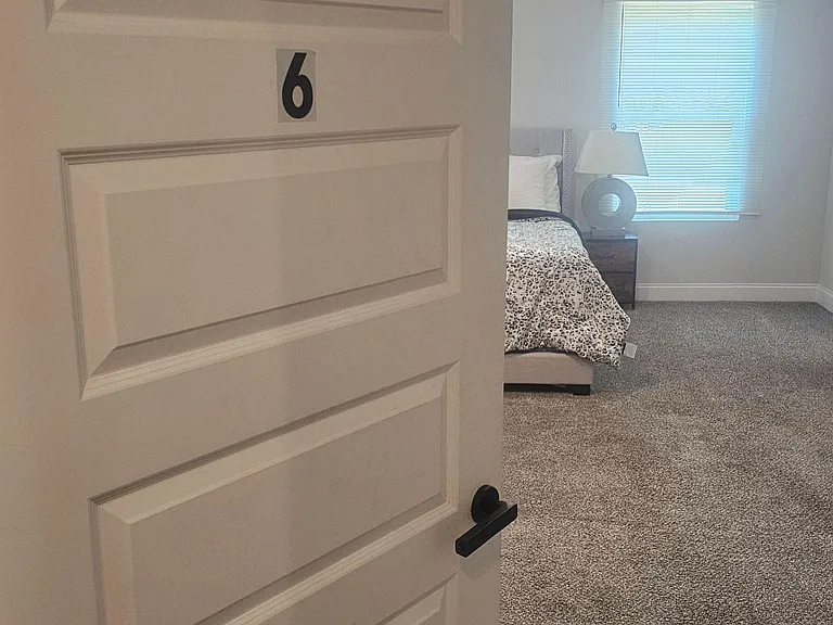 Carpeted bedroom with a large window, recessed lighting, and space for a full bed plus nightstand.