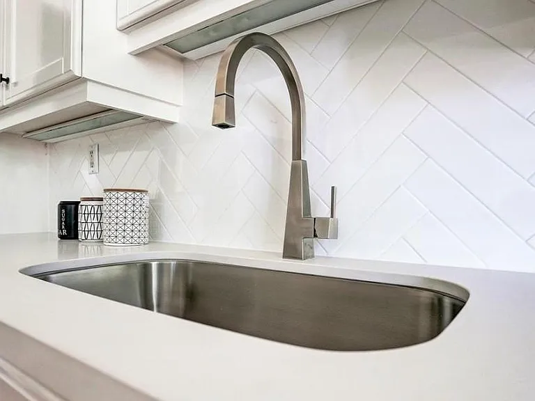 Notice the herringbone detail in this white subway tile, accompanied with a large single basin stainless steel sink