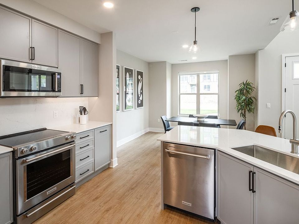 Signature Collection kitchen with stainless steel appliances, white quartz countertop, grey cabinetry, white quartz backsplash, hard surface flooring, and pendant lighting