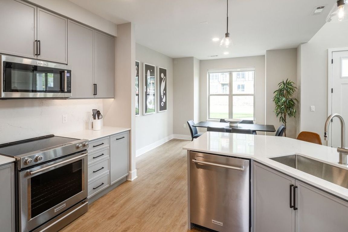 Signature Collection kitchen with stainless steel appliances, white quartz countertop, grey cabinetry, white quartz backsplash, hard surface flooring, and pendant lighting