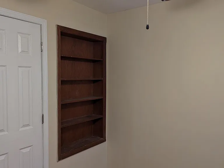 3rd bedroom with built in book case and ceiling fan with ceiling light.