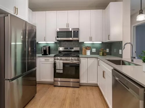 Renovated Package II kitchen with stainless steel appliances, grey quartz countertops, white cabinetry, grey tile backsplash, and hard surface flooring - Avalon at Assembly Row