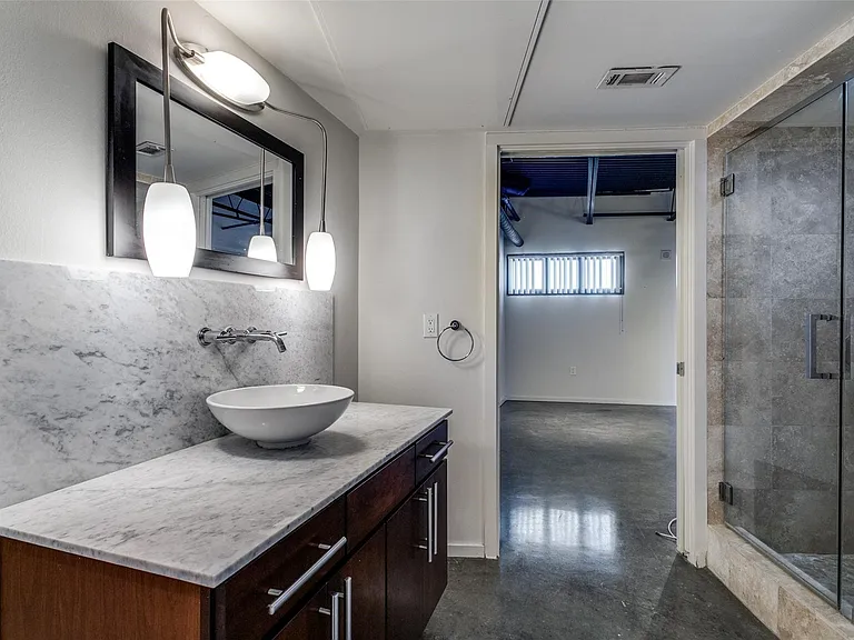Bathroom vanity with wall-mounted faucet, vessel sink, and stone countertop with matching backsplash