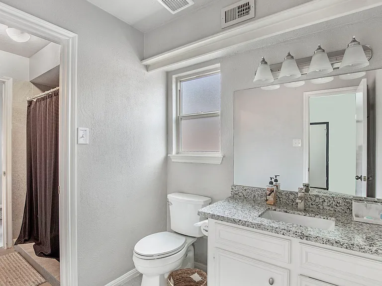 Private half bath with granite-style vanity, large mirror, and a window for natural light plus a shared shower.