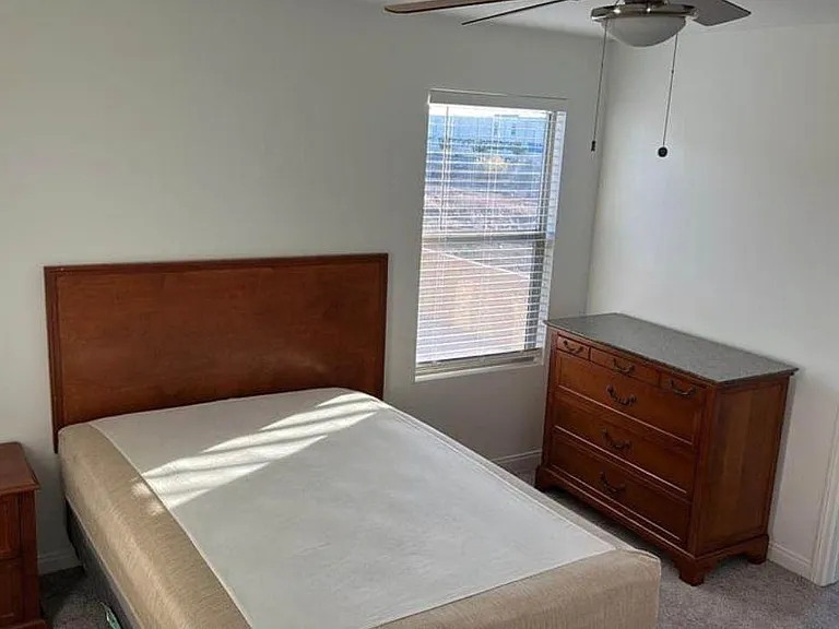 Furnished bedroom with a full bed, nightstand and dresser, plus a window with blinds and a convenient adjacent bath.