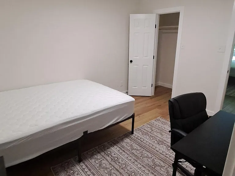 Private bedroom with wood-style floors, area rug, and furnished workspace. Includes a closet for convenient storage.