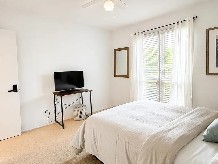 Comfortable bedroom with a large window, ceiling fan, and space for a TV stand or desk setup.