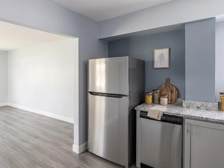 Updated kitchen with granite-look counters, stainless appliances, and ample cabinet space, opening to an adjoining room.