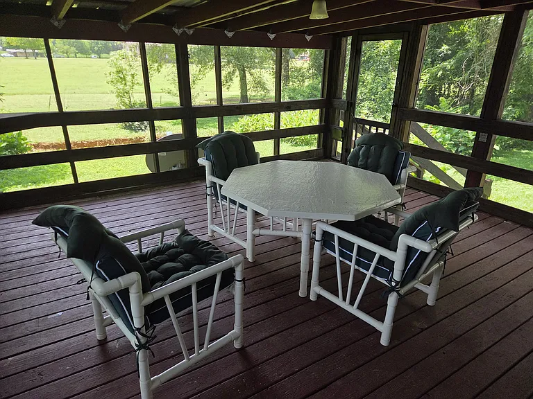 Screened in porch with stairs to backyard and table with 4 chairs and cushions