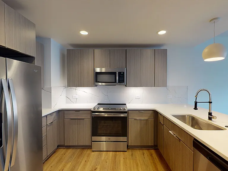Apartment kitchen with stainless steel appliances, quartz countertops and wood-style flooring.