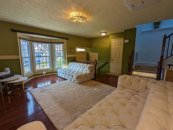 The living room with hardwood floors and panoramic bay window. The doors from left to right are: the main entrance, the guest half-bathroom, and the closet. Furniture/carpet not included.
