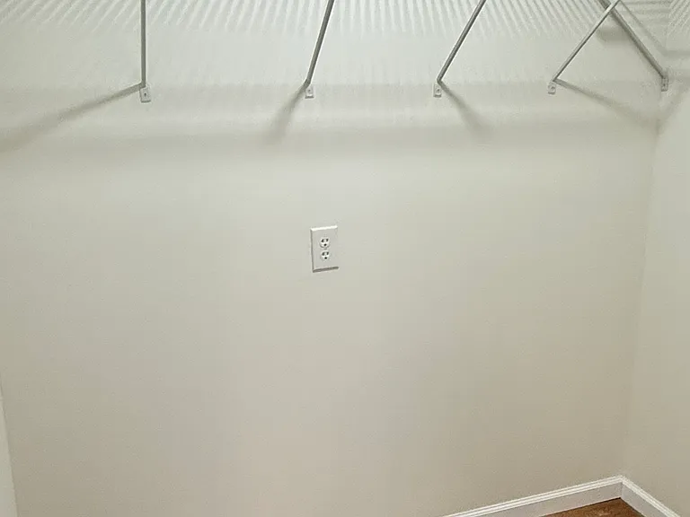 Spacious bedroom featuring two windows with installed curtain rods for plenty of natural light, a ceiling fan with light, attractive flooring, and a large walk-in closet with built-in shelving for generous storage.