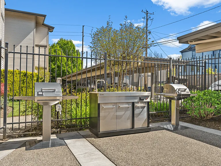 Bright outdoor patio with a round table, chairs, and an ornamental umbrella beside stainless steel grills.