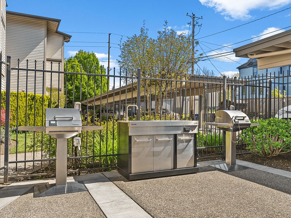 Bright outdoor patio with a round table, chairs, and an ornamental umbrella beside stainless steel grills.