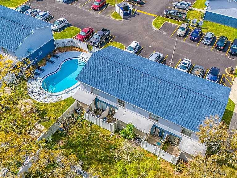 Aerial view of a charming apartment complex featuring a sparkling pool, inviting patios, and ample parking with lush greenery.