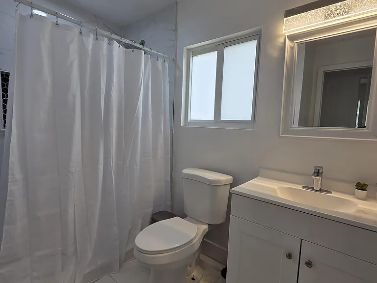 Updated full bath with tiled shower, vanity storage, and a frosted window for natural light and privacy.