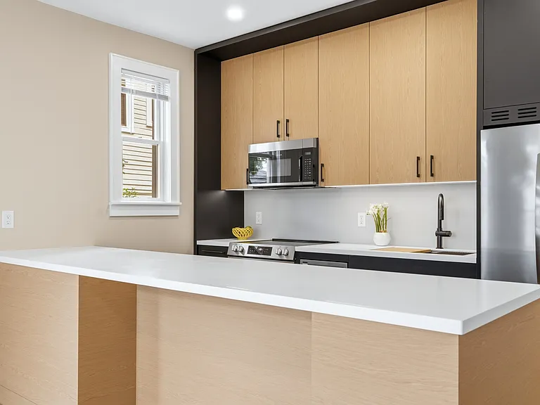 Contemporary kitchen featuring two-tone cabinetry, stainless steel appliances, white countertops, chef's sink, and light wood-finish floorin