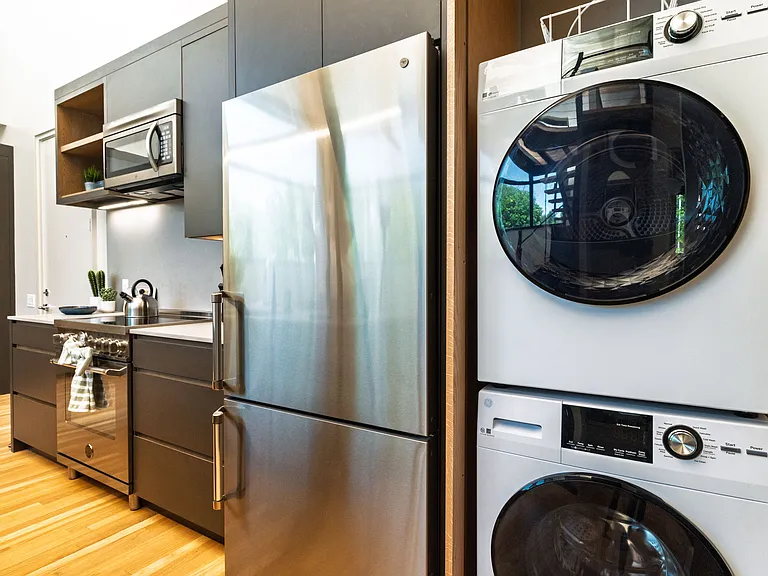 Stackable washer and dryer tucked behind a cabinet in the kitchen, next to the fridge.