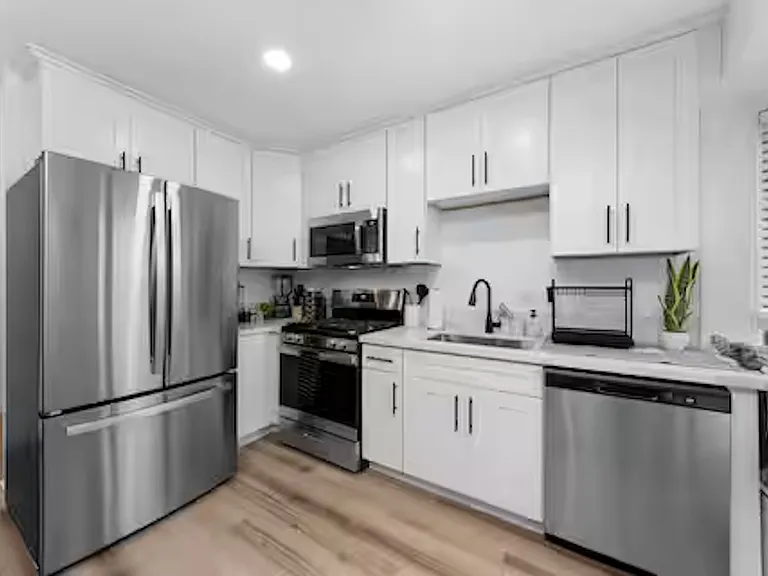 Modern kitchen with white cabinetry, stainless steel appliances, and stone benchtops, featuring a coffee machine, blender, stove cooktop, and plenty of natural light.