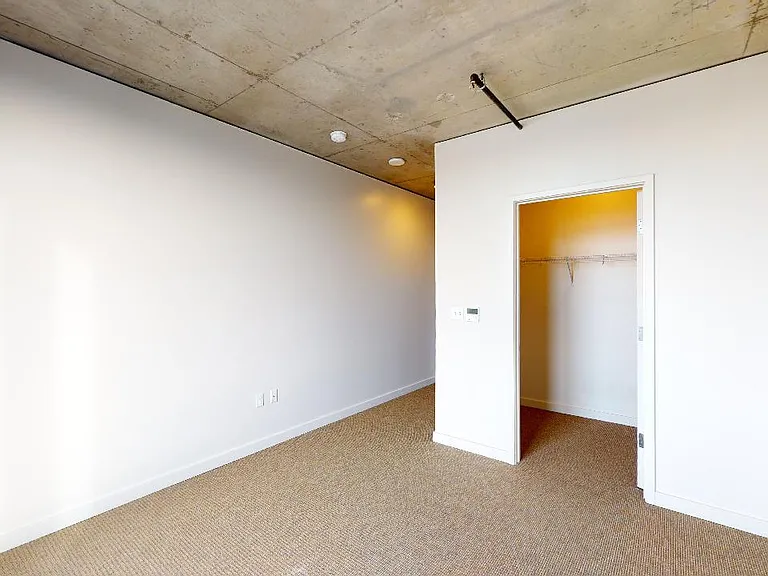 Spacious apartment bedroom with large closet and plush carpet flooring.