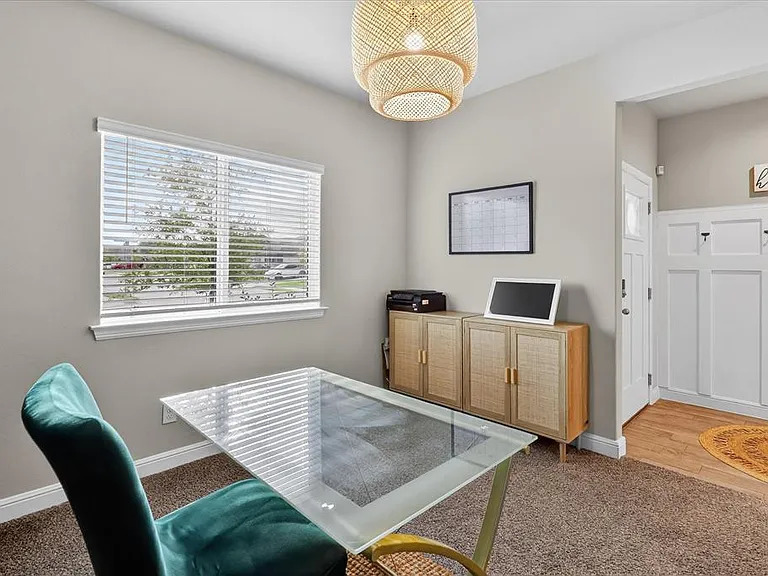Versatile interior space featuring neutral wall paint, a window with horizontal blinds, and a woven pendant light fixture