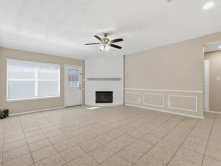 Unfurnished living room featuring ceiling fan, light tile patterned flooring, a large fireplace, and a decorative wall