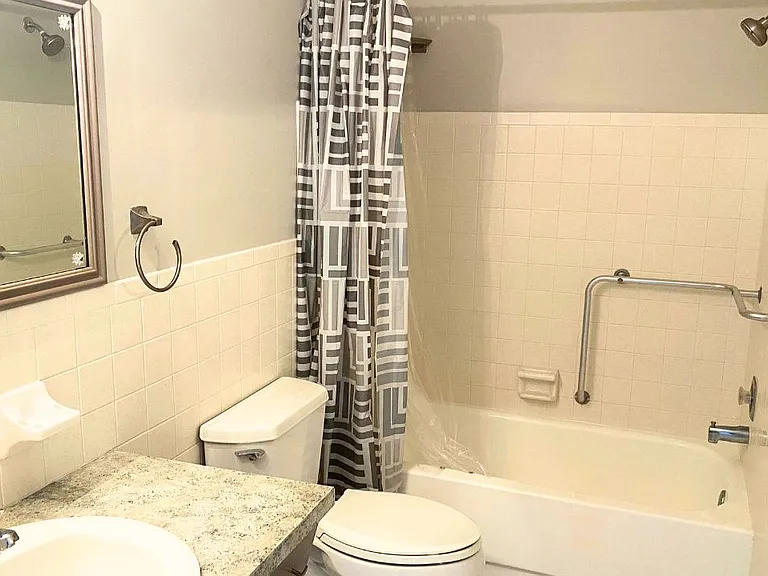 Hallway bathroom comes with bath/shower with safety bars, toilet, sink, and medicine cabinet