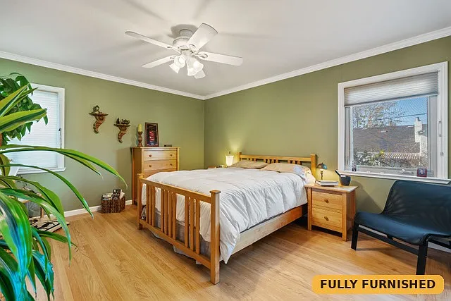 Large bedroom on the main level with 3 windows, a queen bed, ceiling fan, reading chair, two dressers and a large closet with sliding mirrored doors.