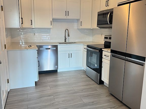 Completely renovated kitchen with new shaker cabinets, stainless steel appliances, subway tile backsplash, modern lighting, and wide-plank gray tile flooring. Fresh, modern, and ready for use.