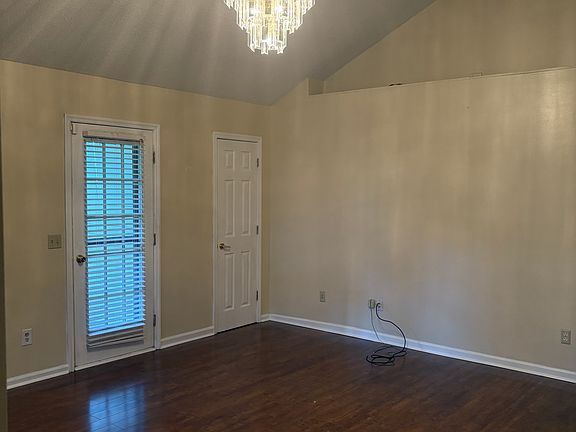Spacious living room with vaulted ceiling, hardwood floors, wood beam, and chandelier.