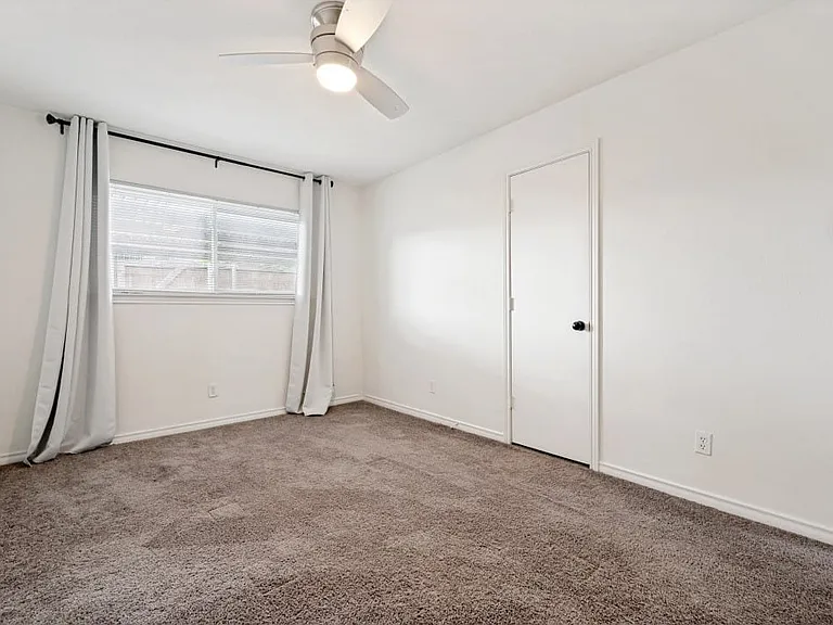 Carpeted room featuring a ceiling fan with integrated lighting, white walls, and a window with horizontal blinds