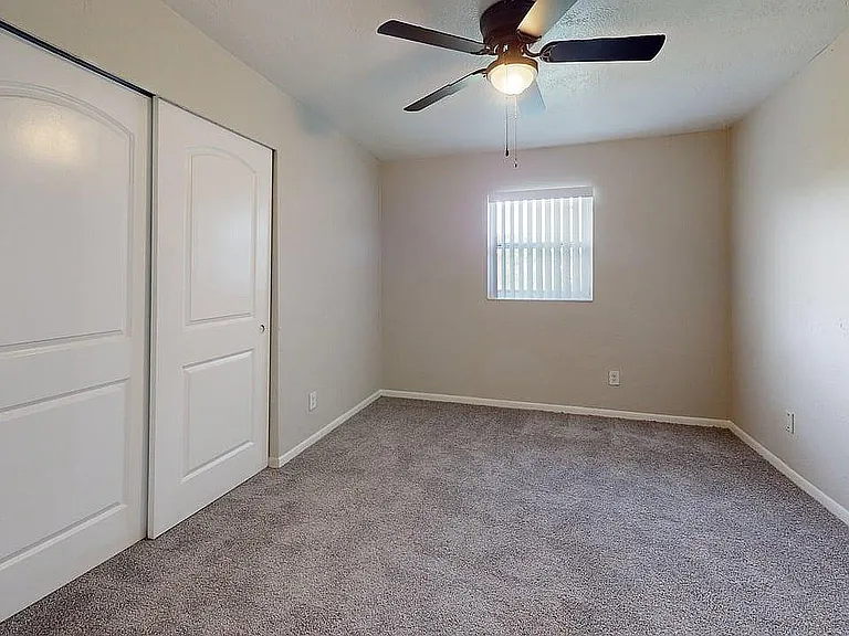 Bright and cozy bedroom with plush carpet, stylish ceiling fan, and ample closet space, offering a serene and inviting atmosphere.