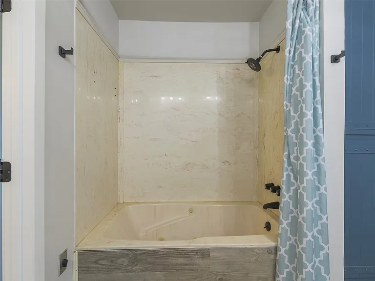 Tub/shower combination featuring a light-toned surround and dark-finish fixtures, complemented by a wood-finish tub skirt