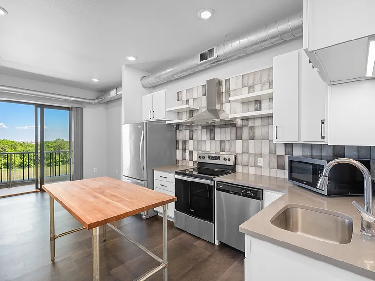 Modern kitchen with stainless steel appliances, spacious wooden island, and scenic balcony view enhancing natural light. Modern kitchen with stainless steel appliances, spacious wooden island, and scenic balcony view enhancing natural light.