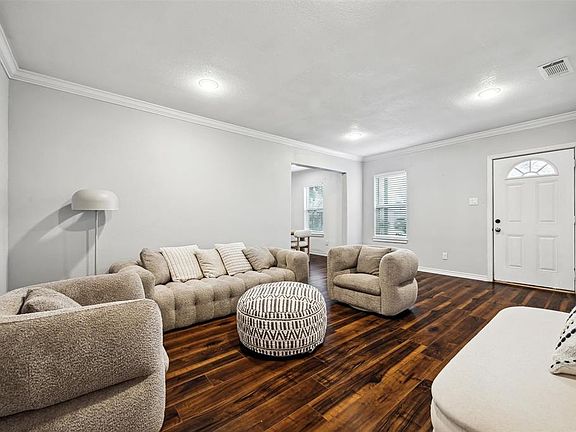This welcoming living room features elegant floors and soft neutral walls. It's well-lit with ample natural light from a window near the entrance, creating a warm, inviting atmosphere.