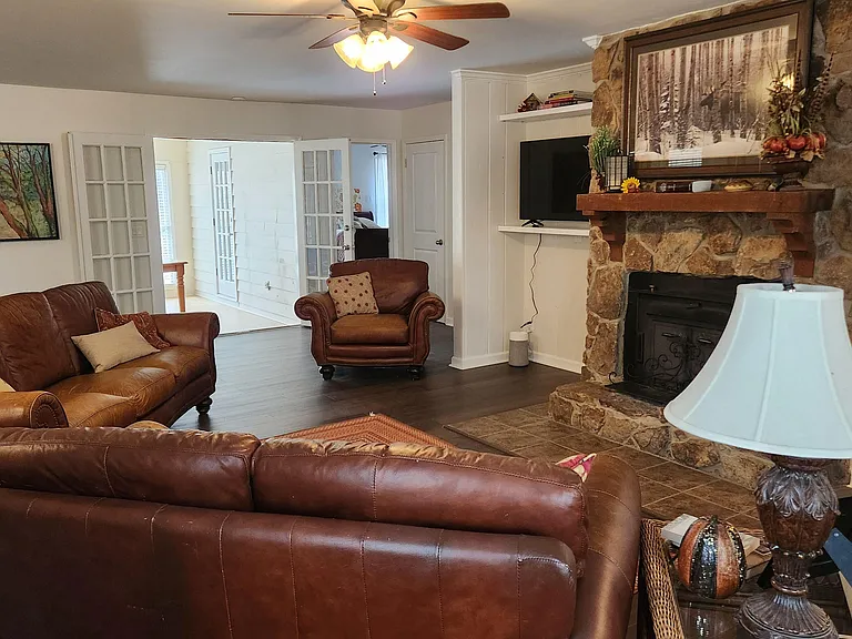 Spacious living room with leather seating, a stone fireplace with mantel, and easy flow to adjacent rooms.