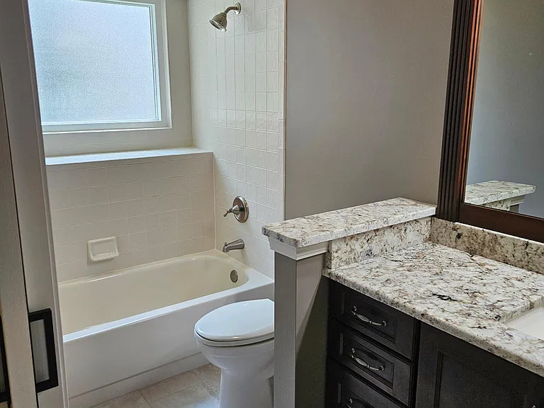 Bedroom 2 bathroom with shower/tub combo, extended tile ledge, granite counters, and full size cabinetry.