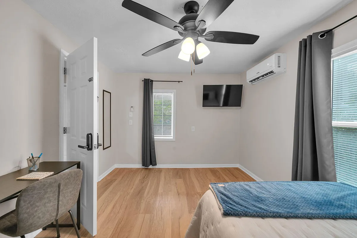 Well-kept bedroom with wood-look floors, ceiling fan with light, window treatments, wall-mounted TV, and mini-split A/C. - Marnie Lane 1/2