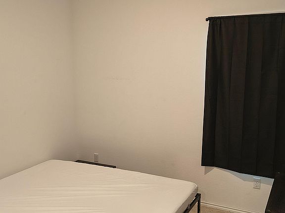 Private bedroom with a bed frame and nearby outlets, plus a window with blackout curtains for added privacy.