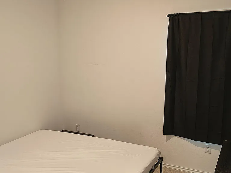 Private bedroom with a bed frame and nearby outlets, plus a window with blackout curtains for added privacy.