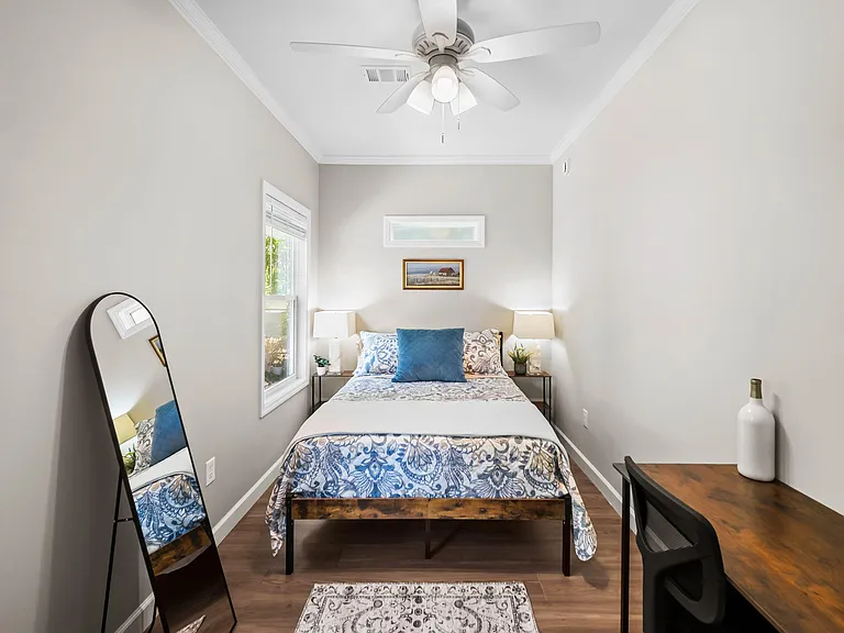 Furnished bedroom with ceiling fan, window for natural light, bedside tables, and a dedicated desk workspace.