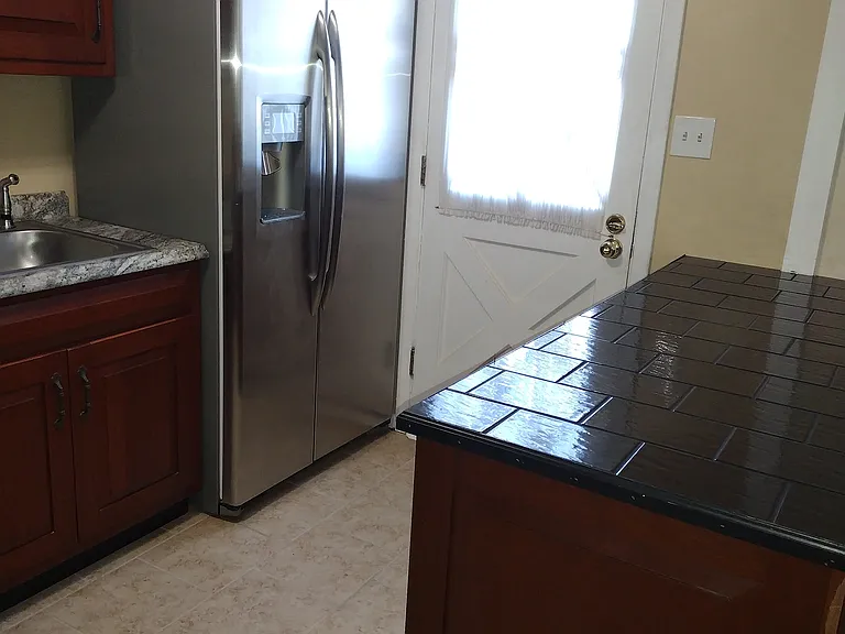 On the right side of the photo is the kitchen island with open storage under the black tile top facing into the kitchen.