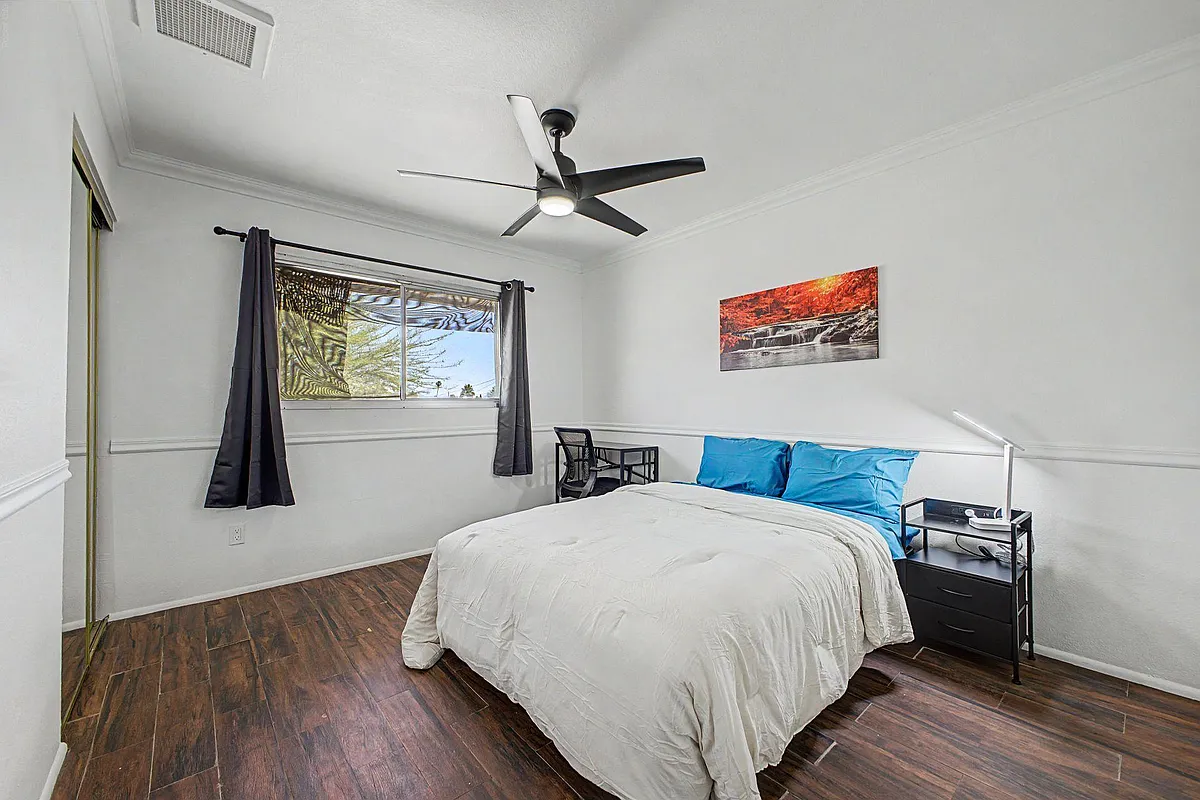 Private bedroom with a queen bed, desk/work area, ceiling fan, and large window with curtains over wood-look floors. - N 42nd Ln