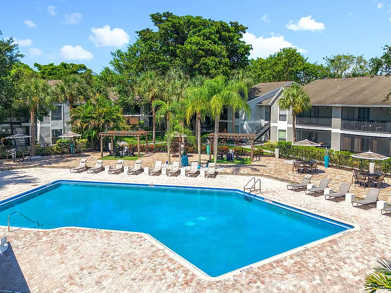Dive into relaxation at our sparkling swimming pool surrounded by lush landscaping, lounge chairs, umbrellas, and shaded pergola seating for a true resort-style retreat.