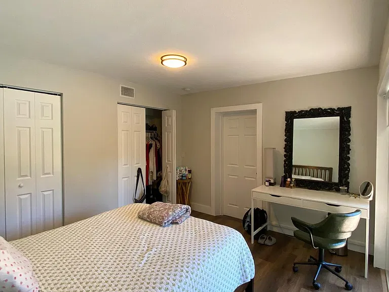 Spacious bedroom with a full bed, wide plank flooring, and a dedicated desk/vanity area plus closet storage.